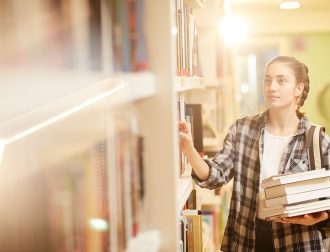 Woman in the library Young woman standing near the shelves with books and choosing one for herself in the library
